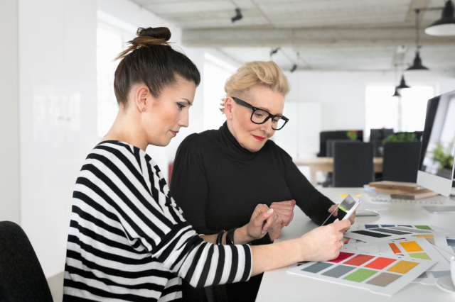 Two creative women looking over a tablet and some swatches.