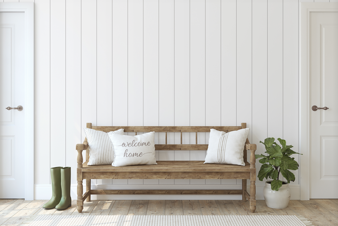 A bright entry way with 3 white pillows (one saying "Welcome Home") atop a wooden bench